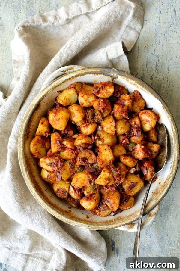 A rustic clay serving dish holds a generous portion of vibrant Patatas Bravas Chilenos, showcasing golden-brown potato cubes coated in a rich, spicy tomato sauce and garnished with fresh herbs, inviting diners to savor its unique Latin American flavors.