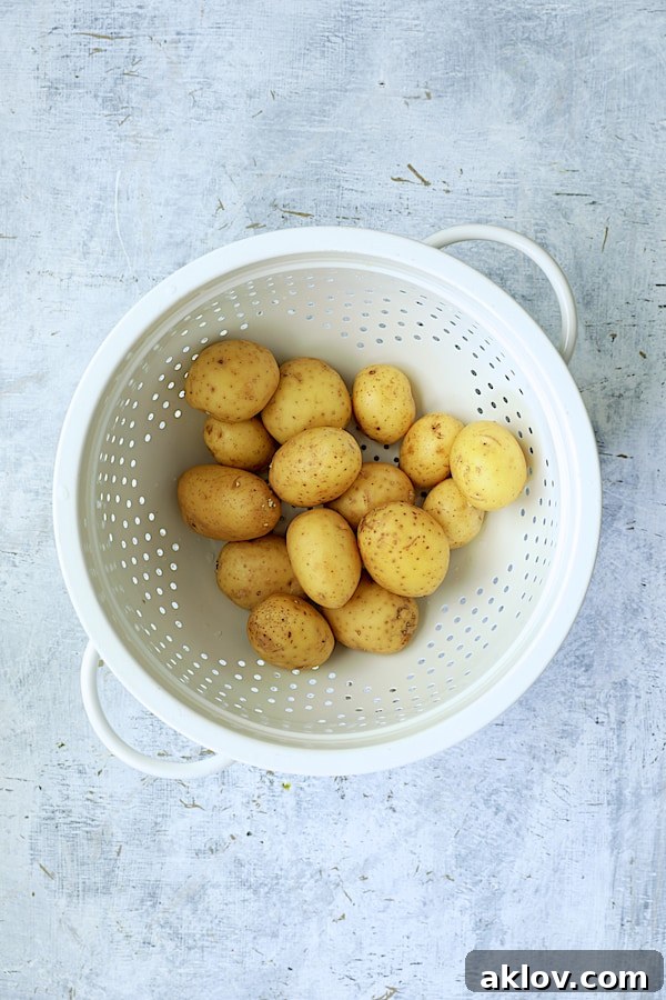 An inviting overhead shot reveals a pristine white colander brimming with freshly washed and prepped potatoes, some halved and others whole, glistening with moisture. The rustic texture of the colander contrasts with the smooth skins of the potatoes, hinting at the delightful meal soon to be created.