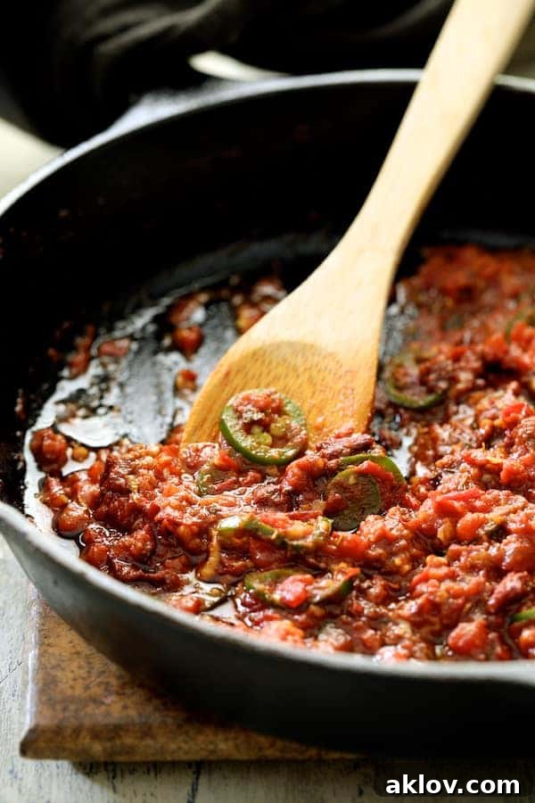 A close-up view of a rich, vibrant red sauce being gently stirred in a sturdy cast-iron skillet, showcasing the simmering tomatoes, peppers, and spices that will bring Patatas Bravas Chilenos to life. The robust texture of the skillet contrasts beautifully with the smooth, bubbling sauce.