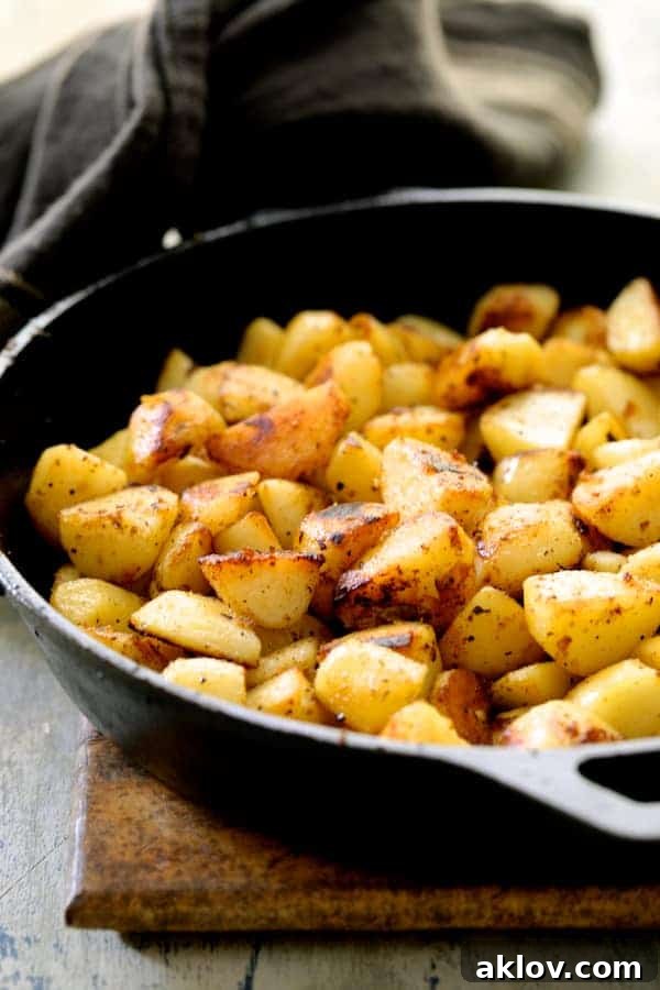 A series of browned, crispy potato cubes are beautifully scattered across the bottom of a well-seasoned cast-iron skillet, exhibiting their golden-brown perfection achieved through careful sautéing. The rustic charm of the skillet enhances the appetizing appeal of the potatoes, ready for the next step in their transformation.