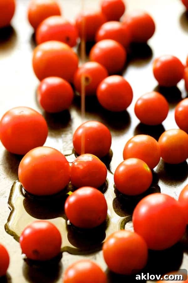 Photo of fresh cherry tomatoes spread on a baking sheet, being drizzled with olive oil before roasting.