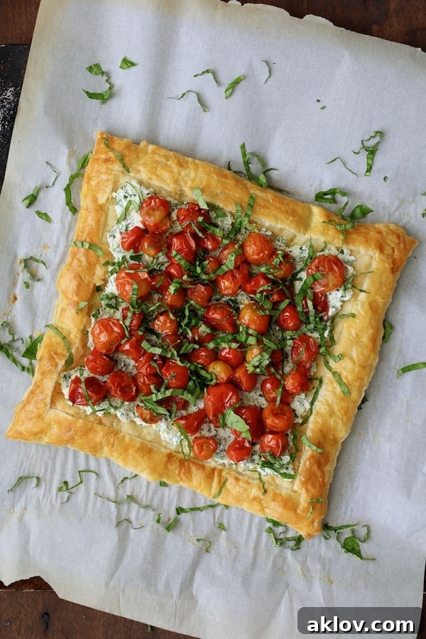 Photo of the tart on parchment paper with additional fresh basil leaves sprinkled over the top as a garnish.