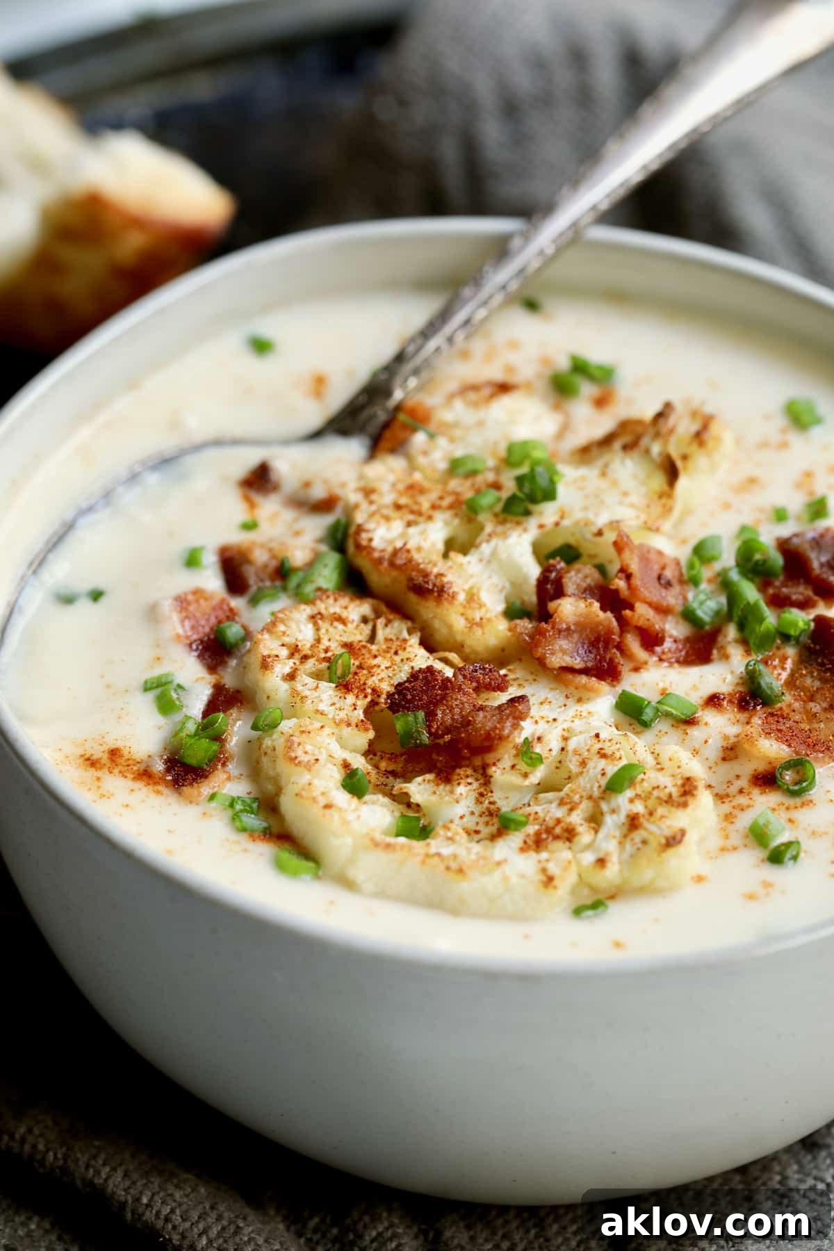 A serving of creamy Cauliflower Potato Soup with Smoked Gouda in a white bowl, elegantly garnished with crispy bacon bits and fresh green chives.