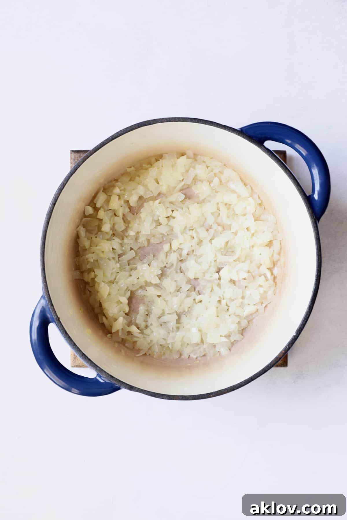 Finely chopped onions are sautéing in a blue Dutch oven, building the aromatic base for the soup.