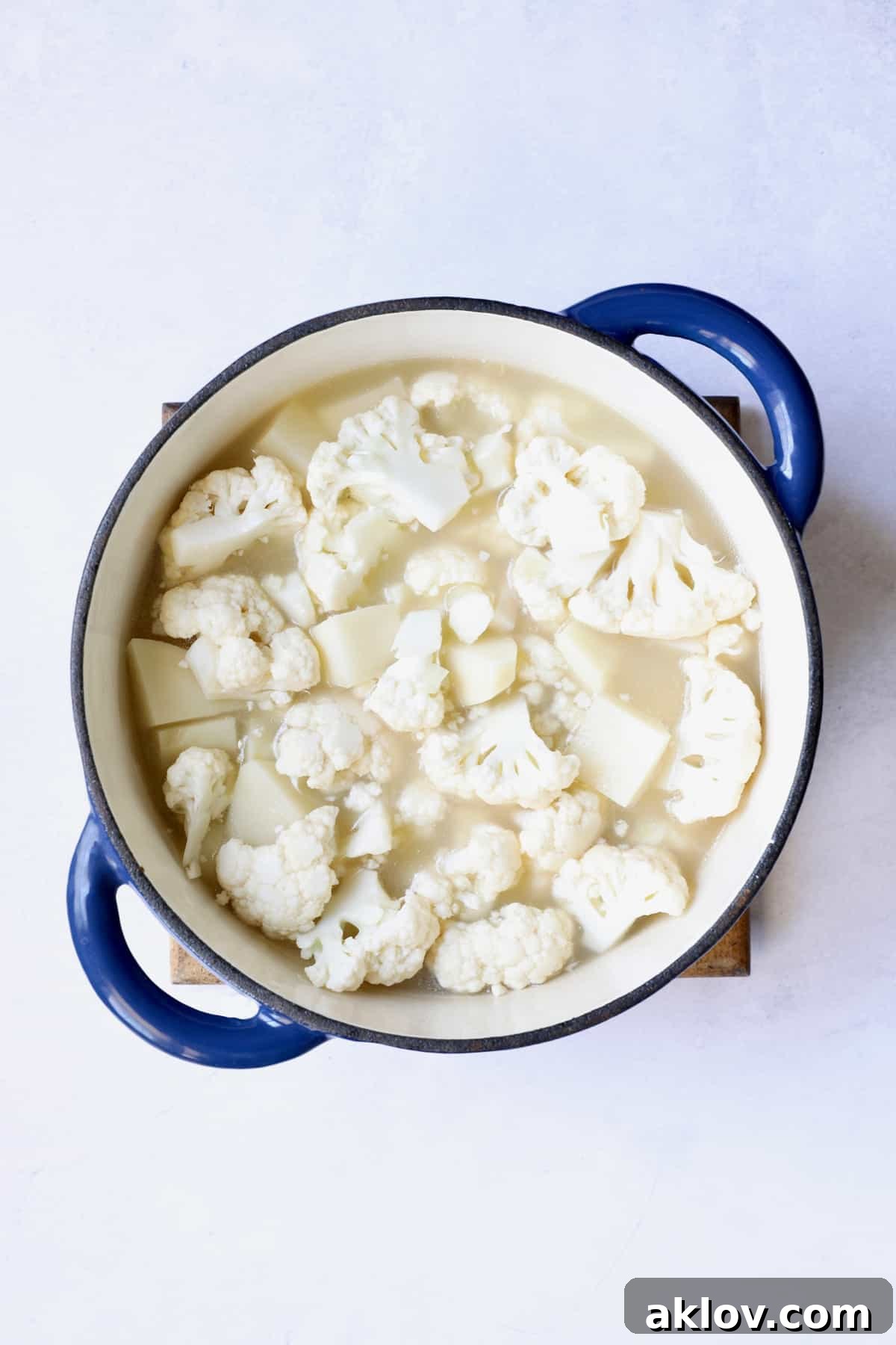 Cubed potatoes and cauliflower florets are simmering gently in a flavorful broth within a blue Dutch oven, becoming tender for the creamy soup.