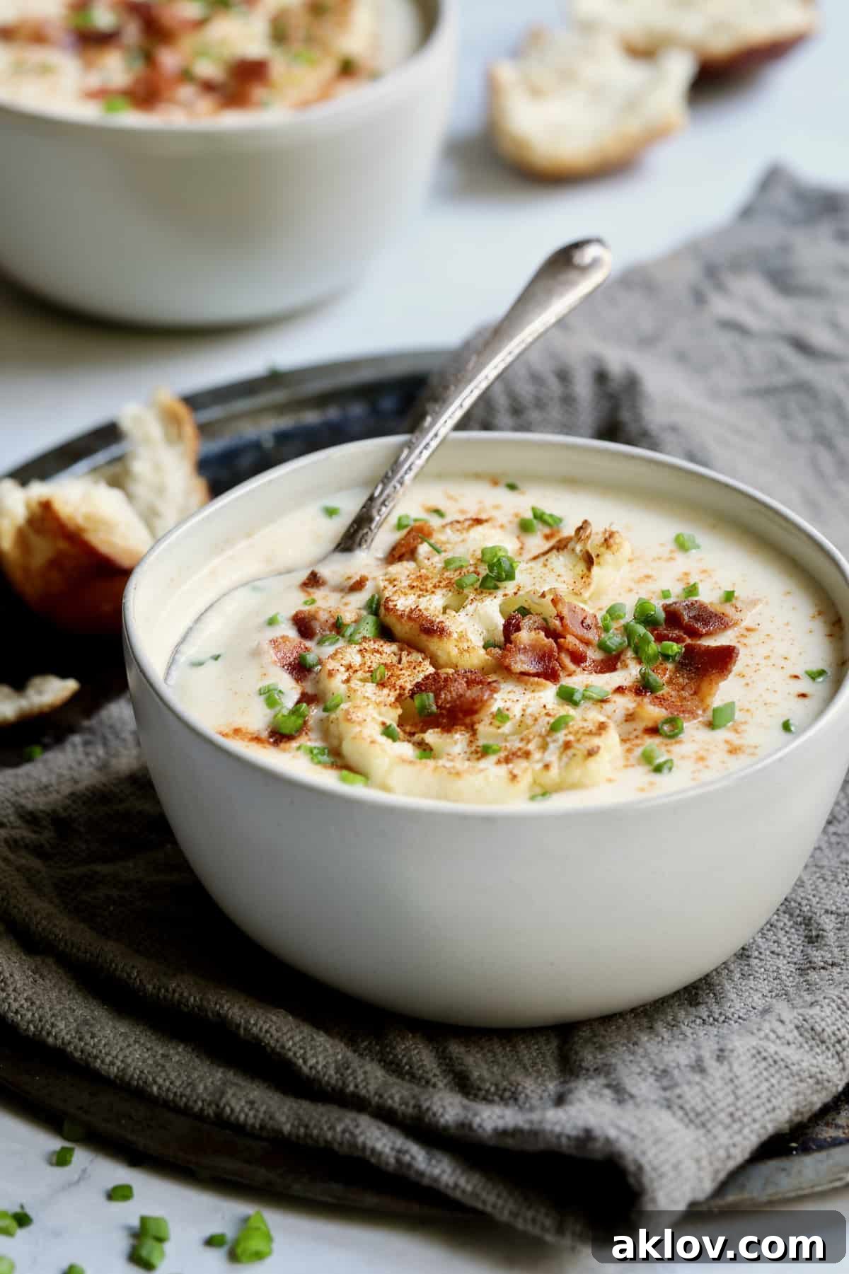 A delectable bowl of Cauliflower Potato Soup with Smoked Gouda, served with a soup spoon and beautifully garnished with roasted cauliflower, crispy bacon, and fresh chives.