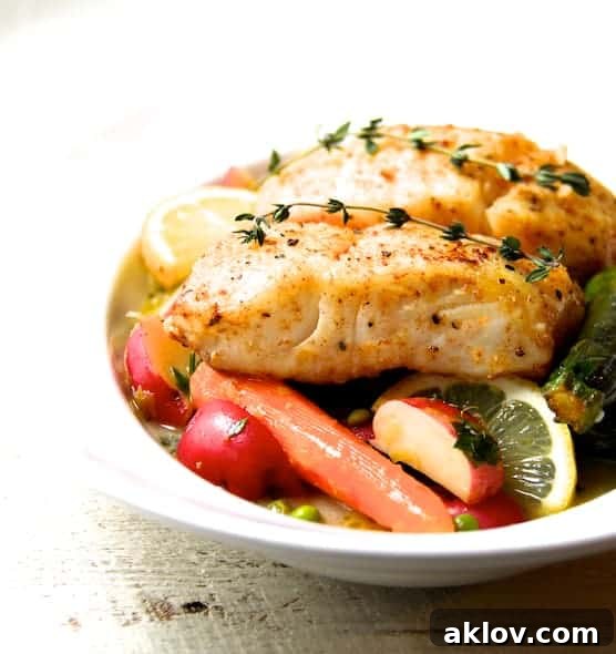 Photo of Butter-Basted Halibut with Lemon-Braised Baby Vegetables in white serving bowl garnished with lemons and thyme.