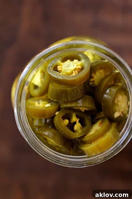 Close-up photo of vibrant green pickled jalapenos in a glass jar, showcasing their texture and color.