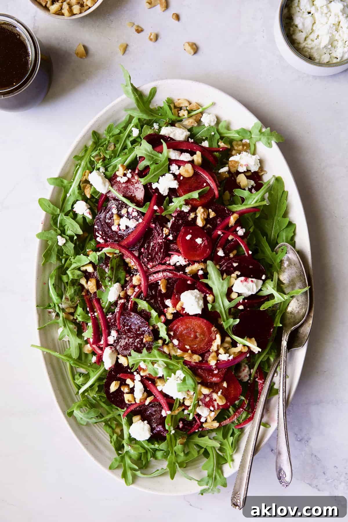 Roasted Beet Salad with Walnuts Goat Cheese and Honey Balsamic Dressing on white oval platter with serving utensils.