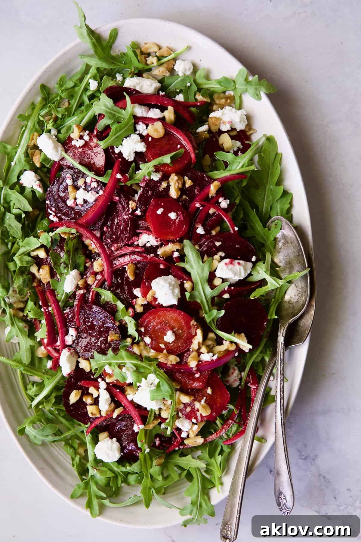 Roasted Beet Salad with Walnuts Goat Cheese and Honey Balsamic Dressing with serving utensils on white oval platter.