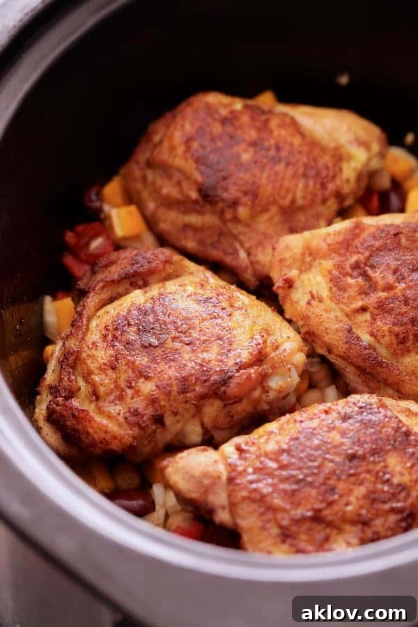 Aromatic Moroccan Chicken Tagine 3 Close-up photo of perfectly browned chicken thighs arranged over a bed of vibrant vegetables and chickpeas inside a slow cooker, ready for the slow-cooking process.