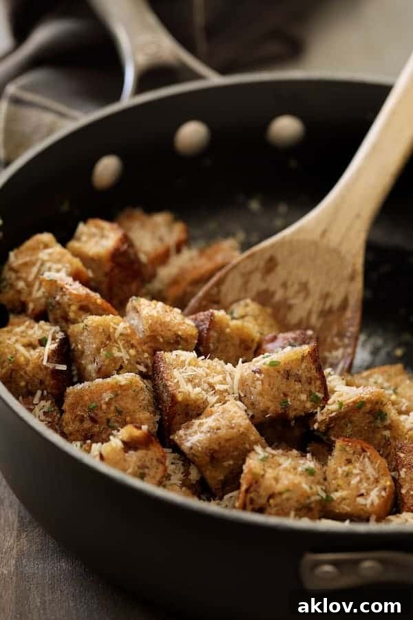 Whole-grain bread cubes being tossed with melted butter, garlic, and fresh herbs in a sauté pan.