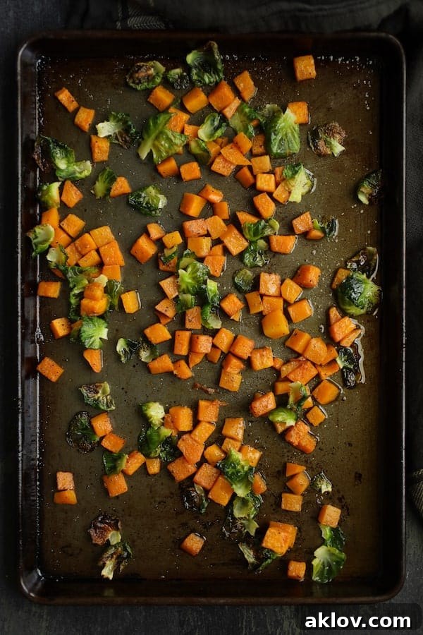 Roasted butternut squash cubes and Brussels sprouts leaves on a baking sheet, golden and tender.