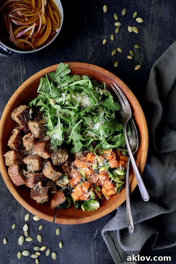 Ingredients for Autumn Panzanella – arugula, warm roasted vegetables, and croutons – arranged in a large wooden bowl before being mixed.