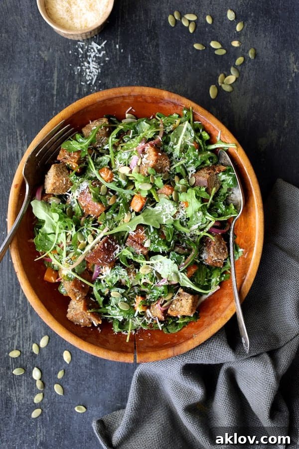 Finished Autumn Panzanella salad in a wooden bowl, garnished with Parmesan cheese and pumpkin seeds.