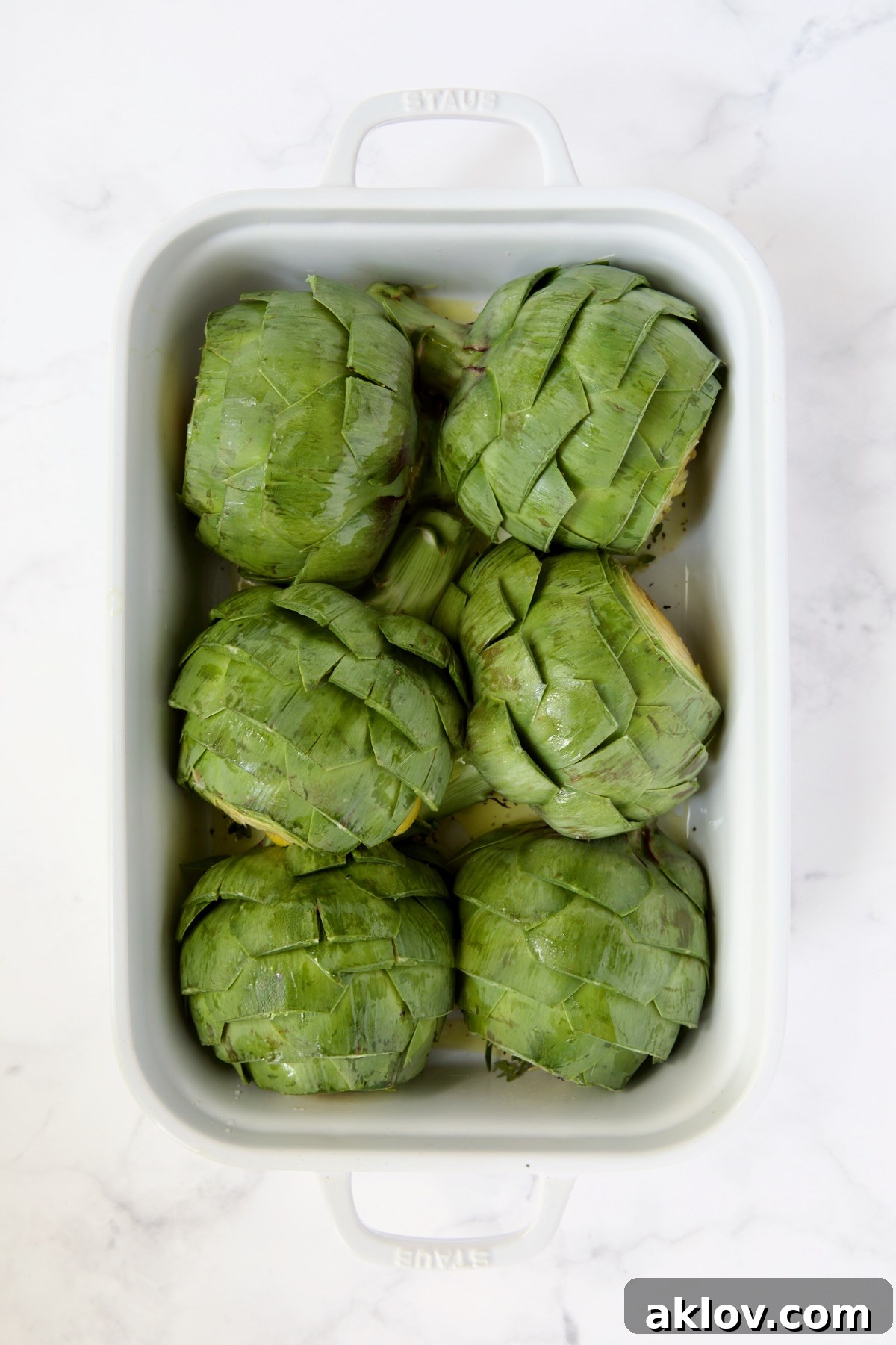 Buttery Garlic Roasted Artichokes 12 Six artichoke halves sitting cut side down in a white roasting pan.
