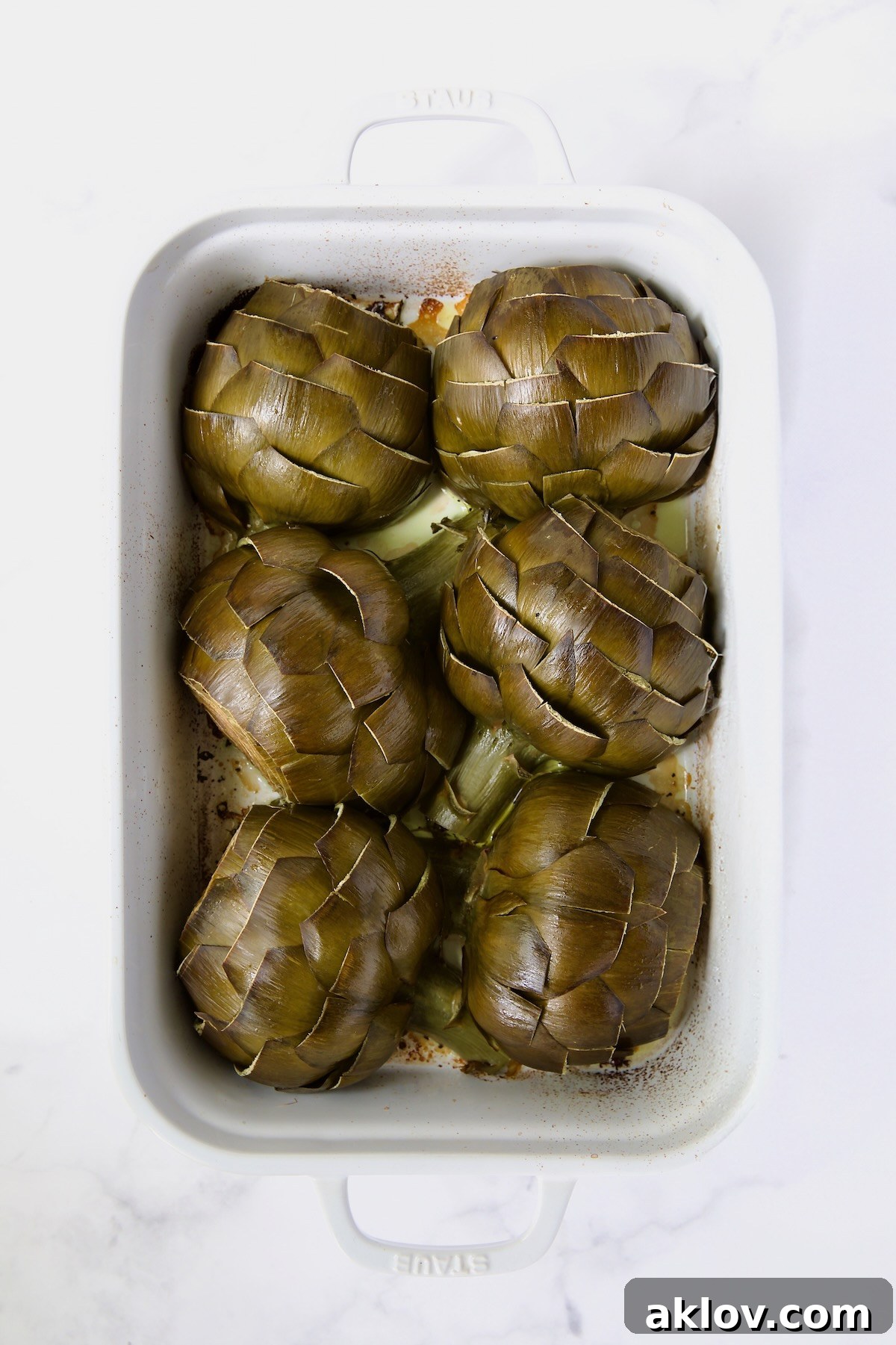Buttery Garlic Roasted Artichokes 13 Six artichoke halves in a white roasting pan with cut side down after being roasted.