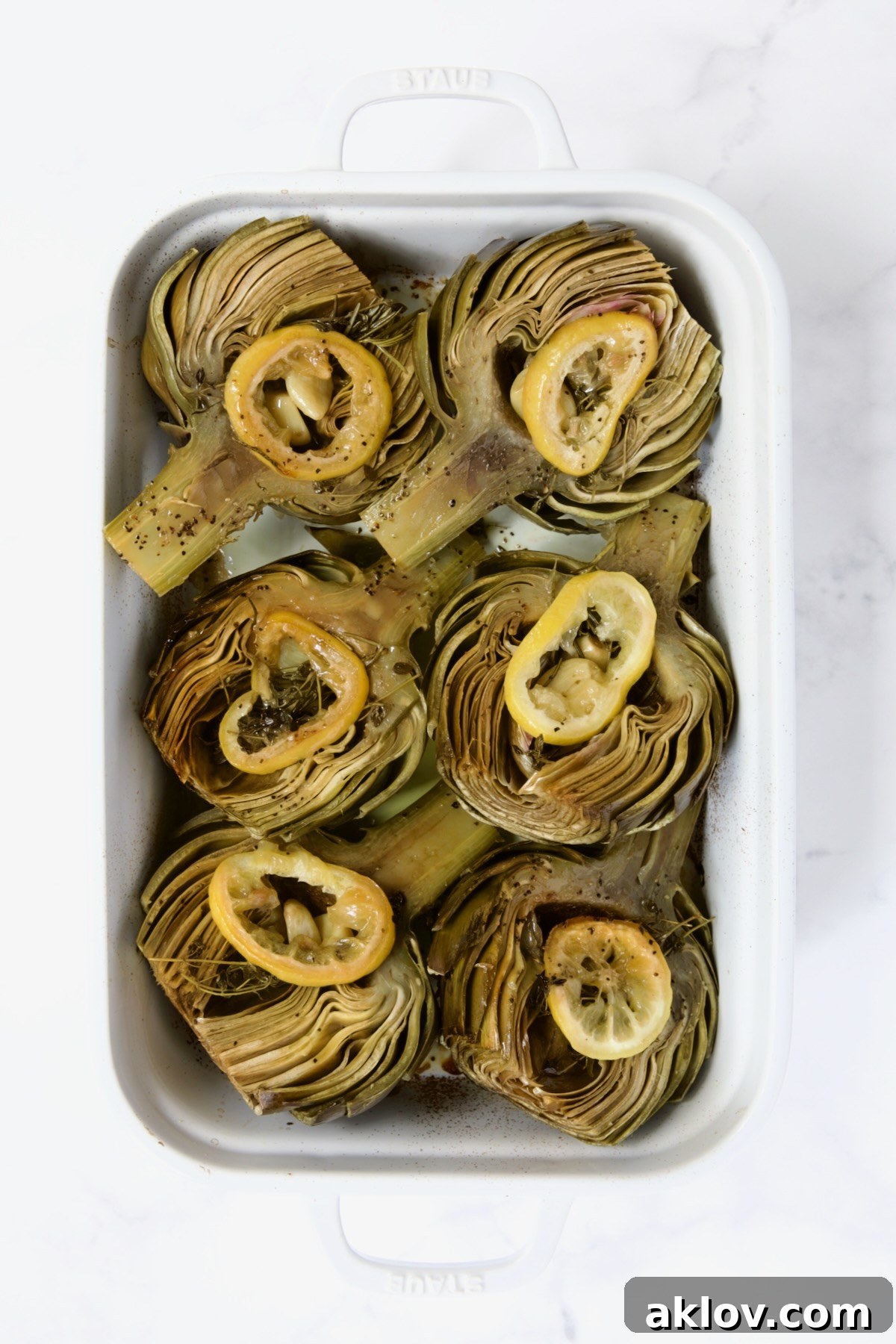 Buttery Garlic Roasted Artichokes 14 Six artichoke halves in a white roasting pan turned cut side up after being roasted.