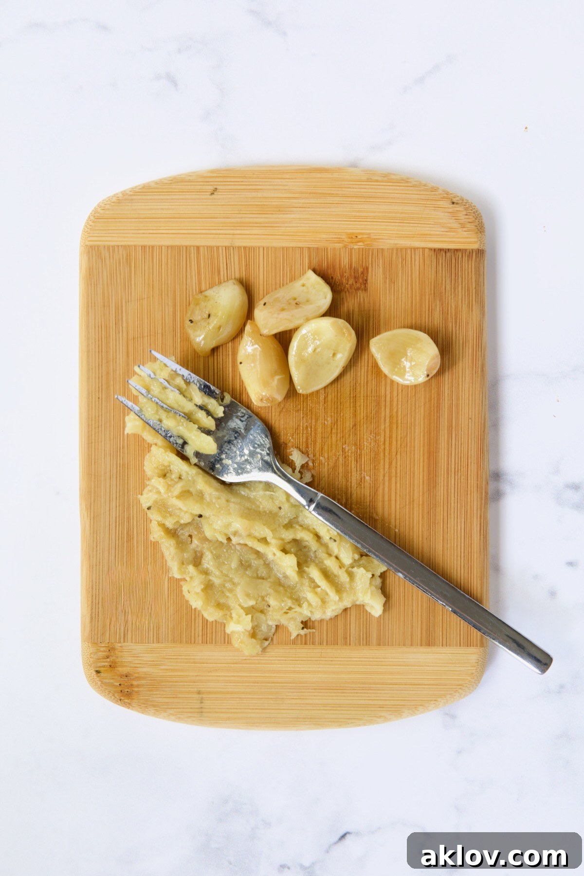 Buttery Garlic Roasted Artichokes 17 Garlic being smashed on bamboo cutting board with fork.