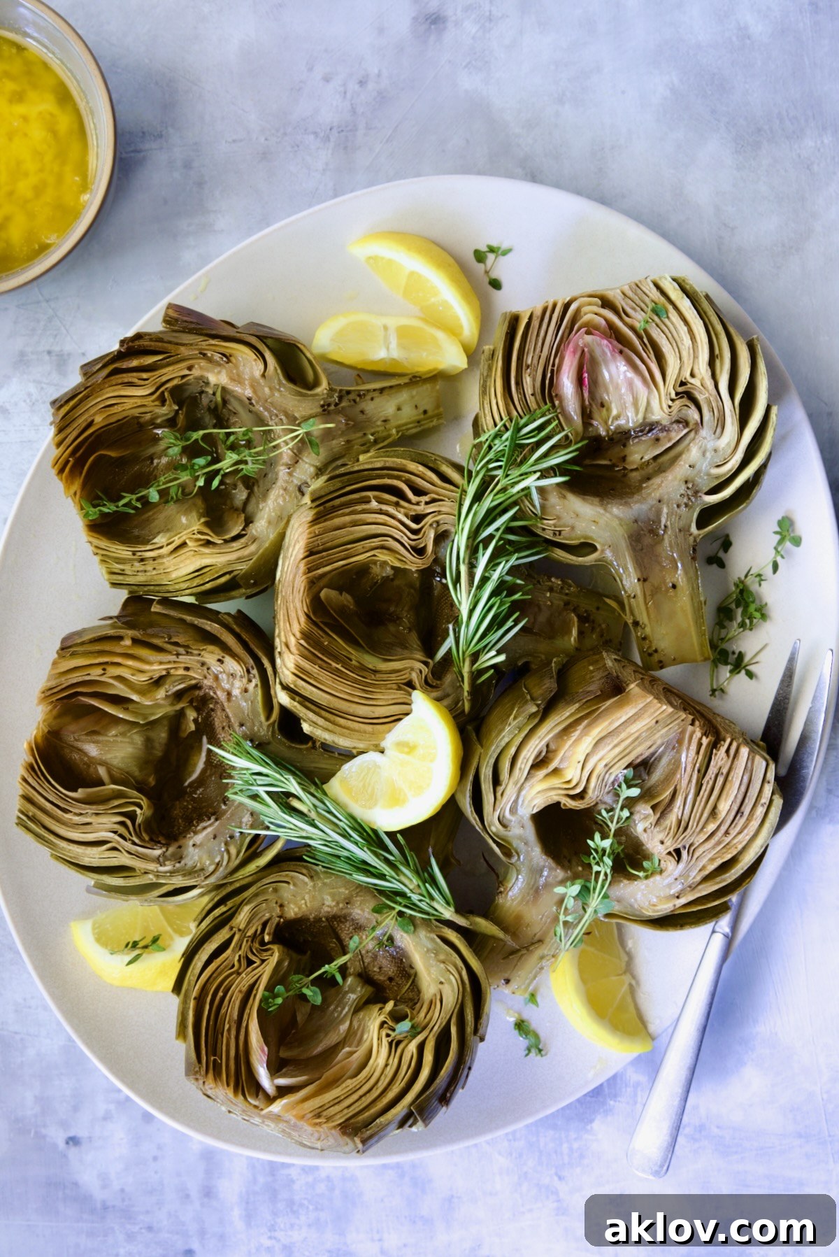 Buttery Garlic Roasted Artichokes 19 Six Roasted Artichoke halves with Garlic Butter garnished with rosemary, thyme sprigs and lemon wedges.