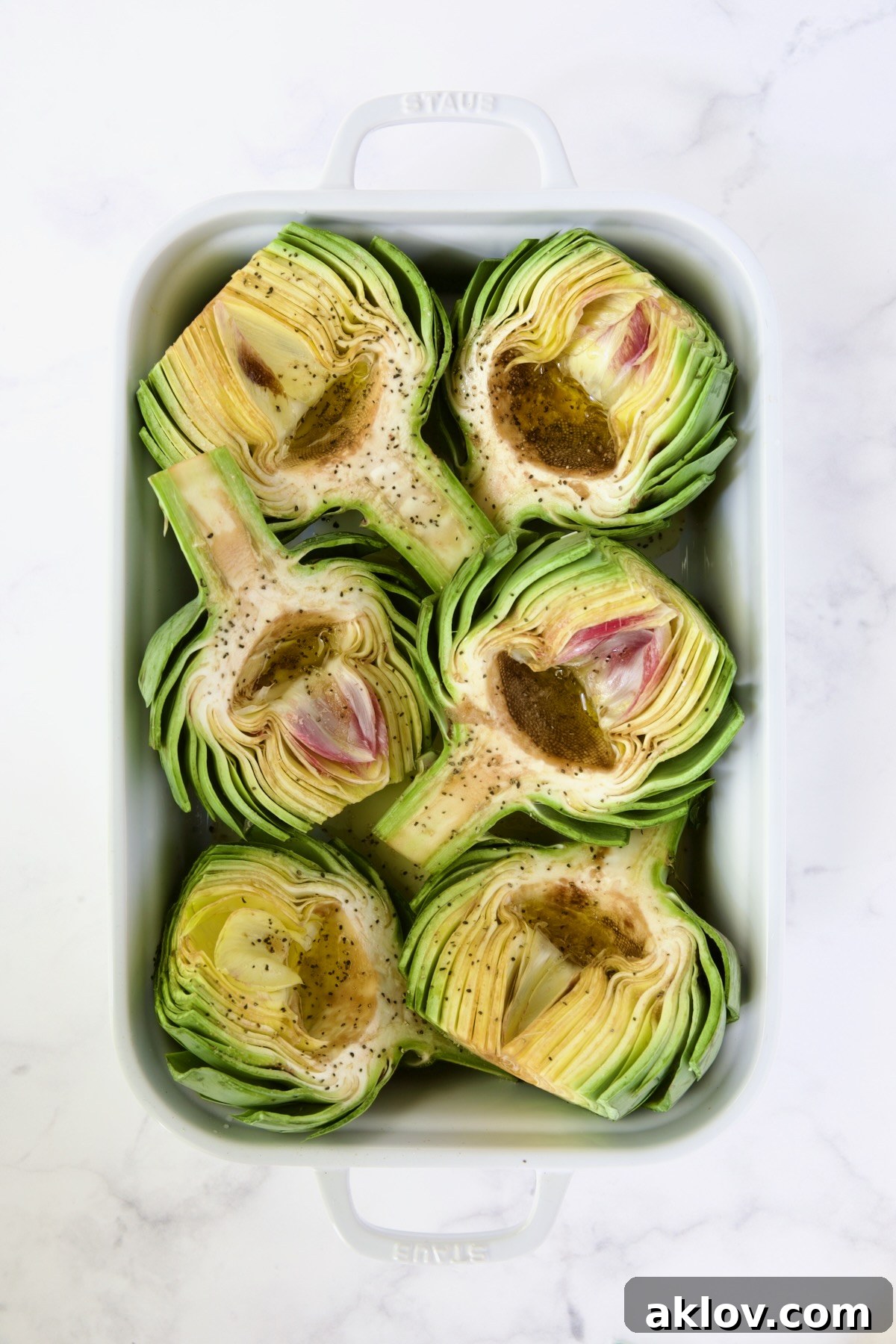 Buttery Garlic Roasted Artichokes 9 Six artichoke halves in a white roasting pan drizzled with olive oil.