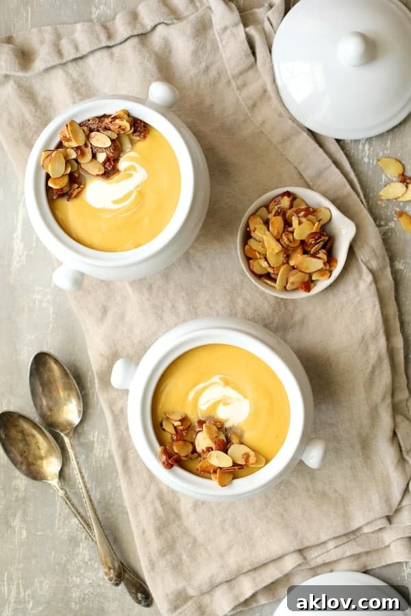 Marsala-Infused Pumpkin Velvet with Mascarpone Swirl 4 Photo of two servings of Pumpkin Soup with Marsala and Mascarpone in bowls on beige napkin with spoons and almond topping.