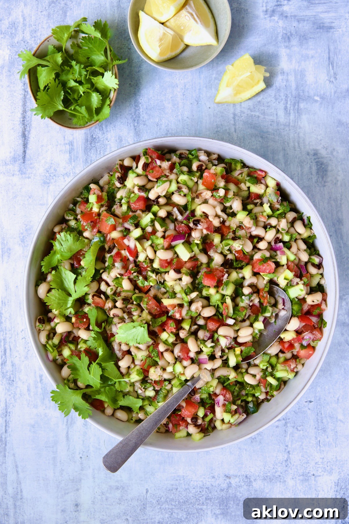 Beautifully presented Black-Eyed Pea Salad in a serving bowl, accompanied by a serving spoon, fresh cilantro sprigs, and bright lemon wedges in small dishes, ready to be savored.