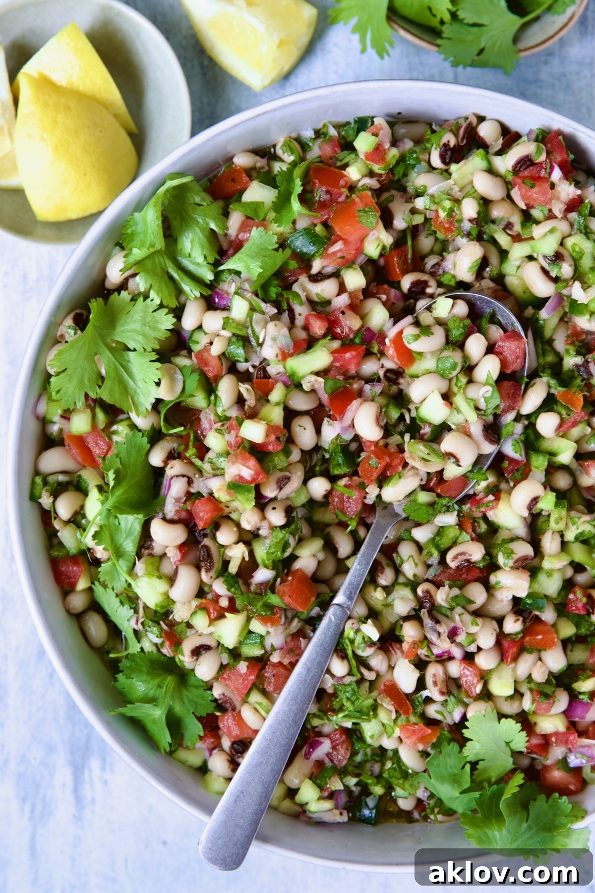 A close-up of the fresh and inviting Black-Eyed Pea Salad in a white bowl, elegantly garnished with lemon wedges and cilantro in smaller bowls, ready to be enjoyed.