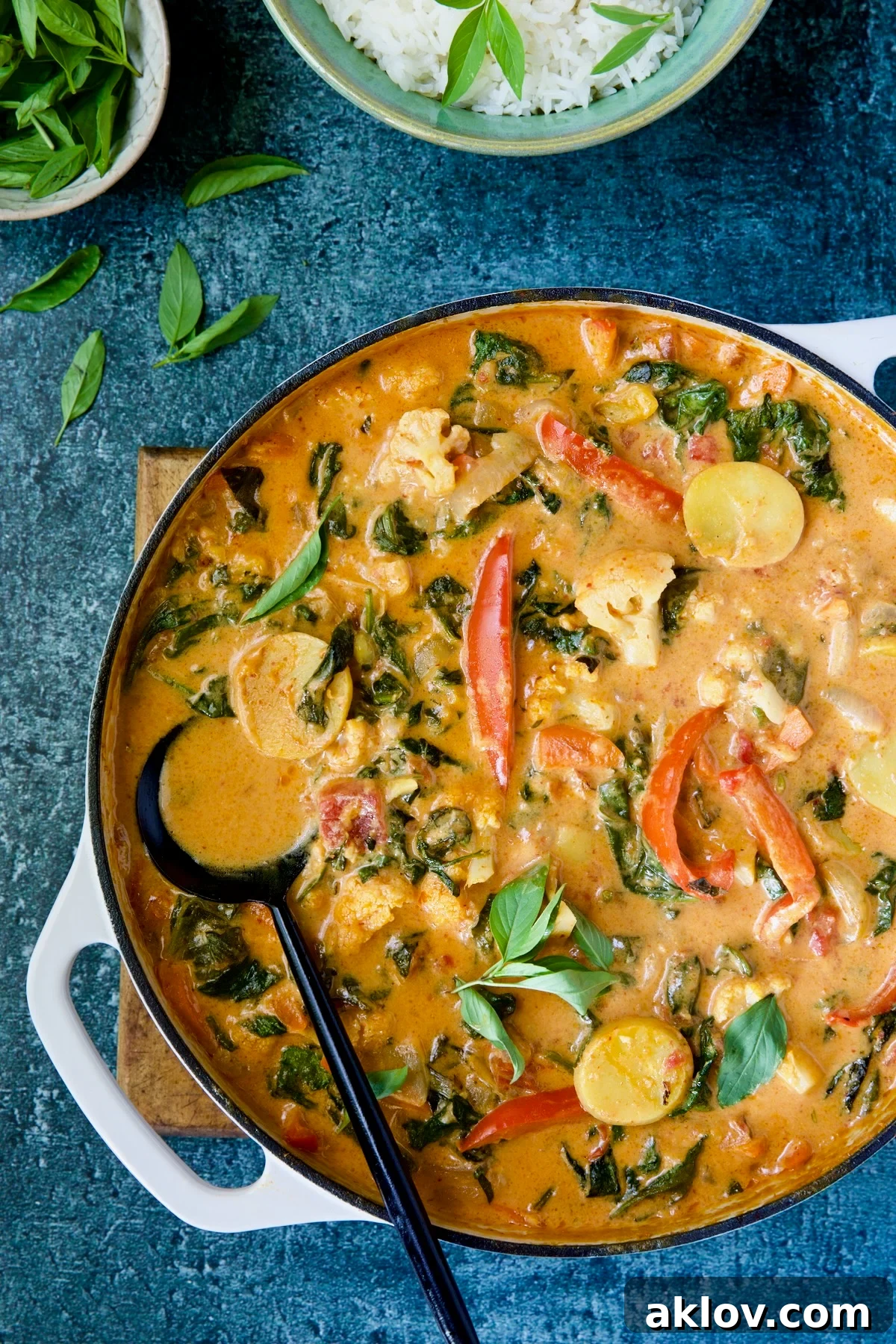 Rich and creamy Vegan Thai Red Curry in a white enamel cast iron skillet, ready to be served with a black spoon.