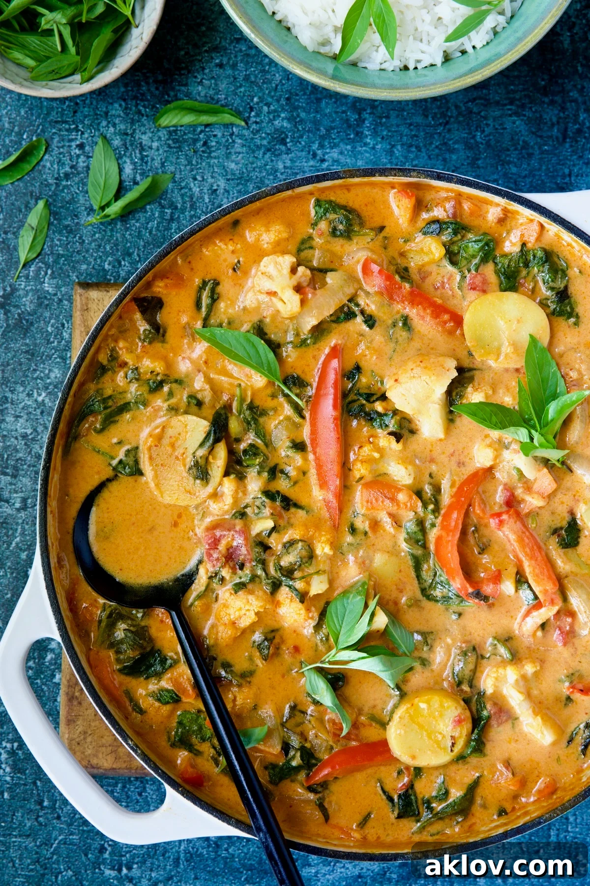 A large serving of Vegan Thai Red Curry in a white enamel cast iron skillet with a black serving spoon, ready to be enjoyed.