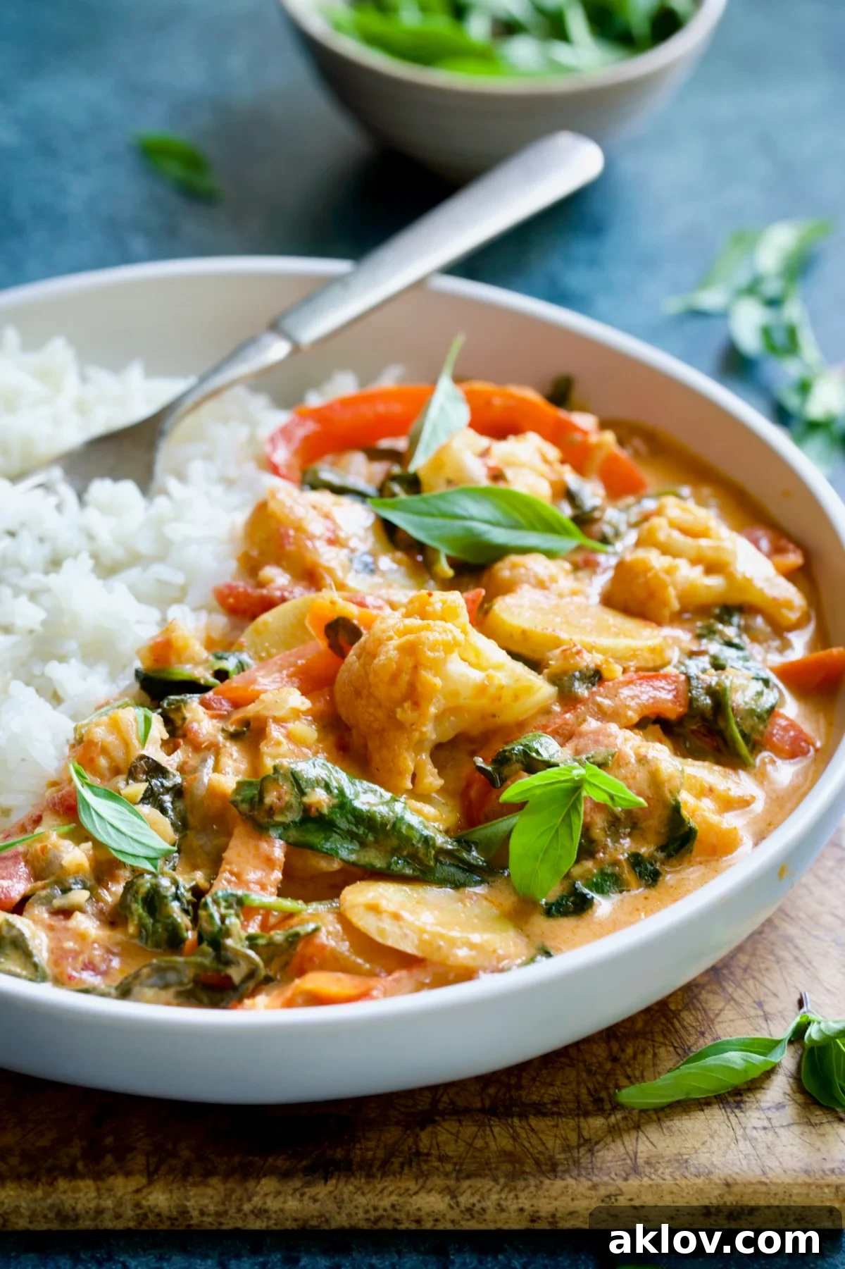 A beautifully plated bowl of vegetable curry with a side of rice, garnished with fresh basil leaves, ready to be eaten.