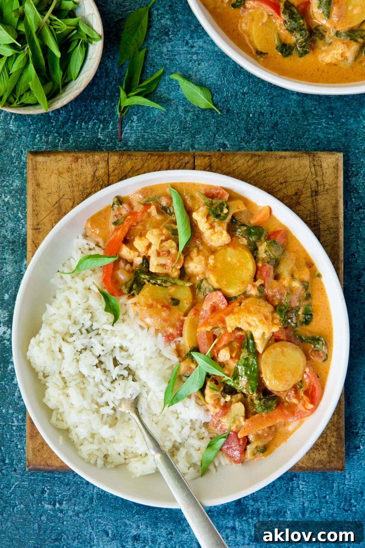 A close-up shot of a bowl of rich vegetable curry with rice, garnished with vibrant fresh basil leaves, emphasizing its appetizing appeal.