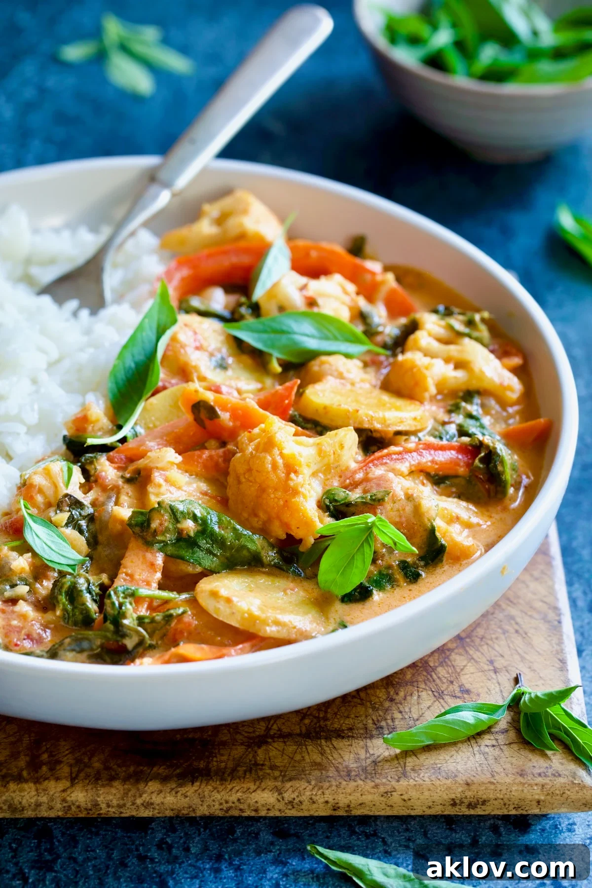 A vibrant bowl of Vegan Thai Red Curry garnished with fresh green basil leaves, highlighting its colorful and appetizing presentation.