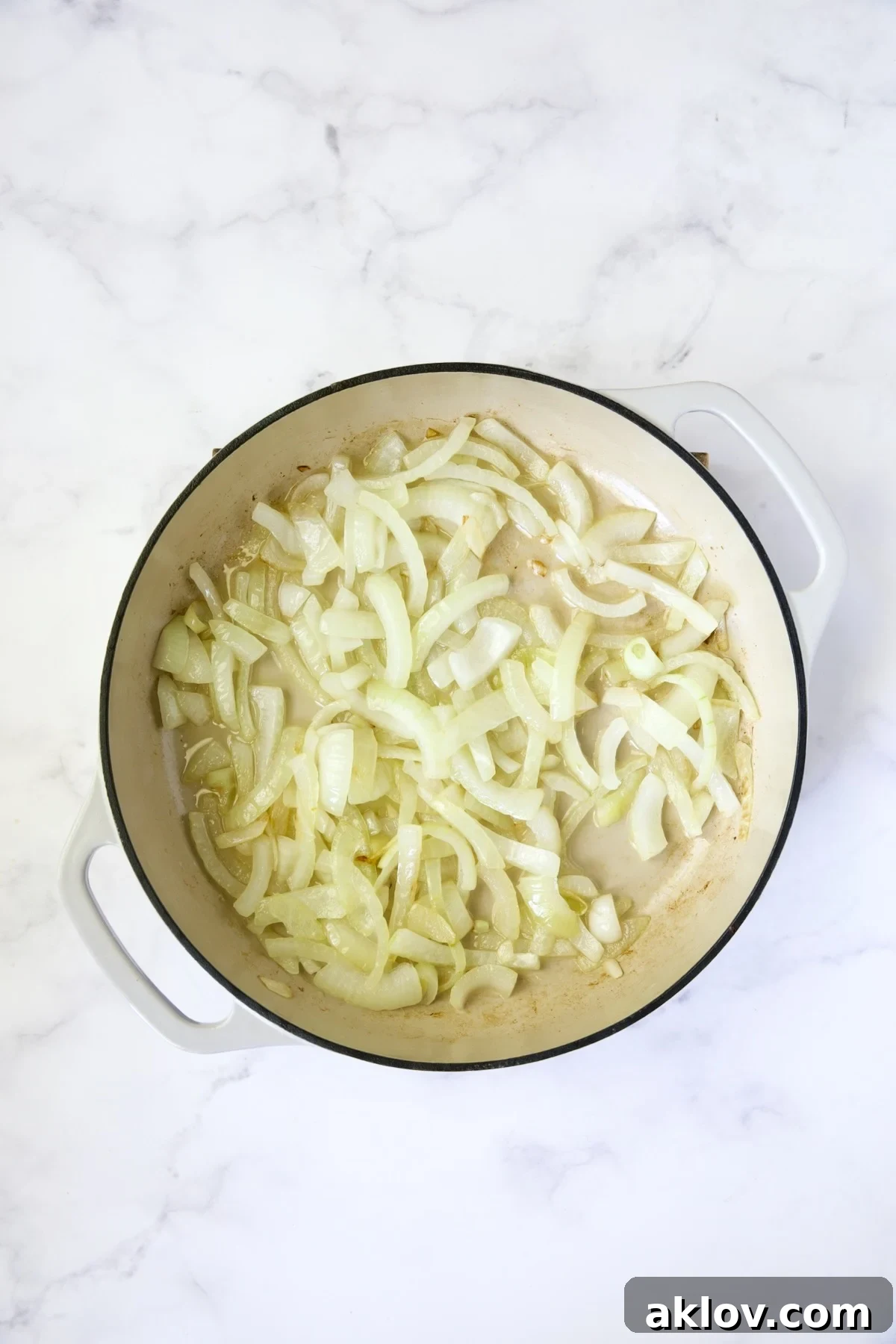 Sliced onions gently cooking in a white enamel cast iron skillet, starting to soften.
