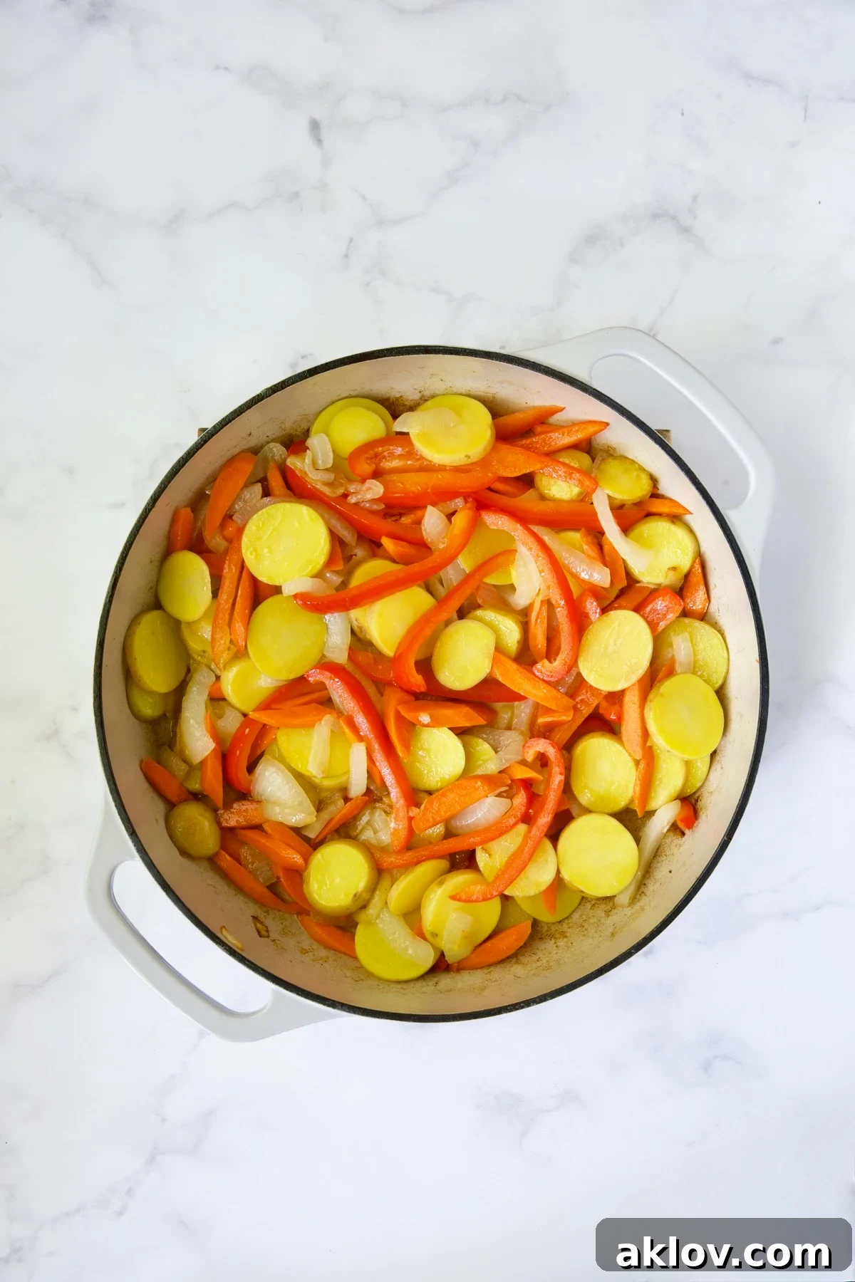 Process shot showing sliced onions, carrots, red bell pepper, and potatoes sautéing in the skillet.