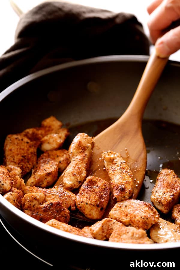 Close-up photo of chicken strips being cooked and stirred in a hot skillet with a wooden spoon, achieving a golden brown sear.