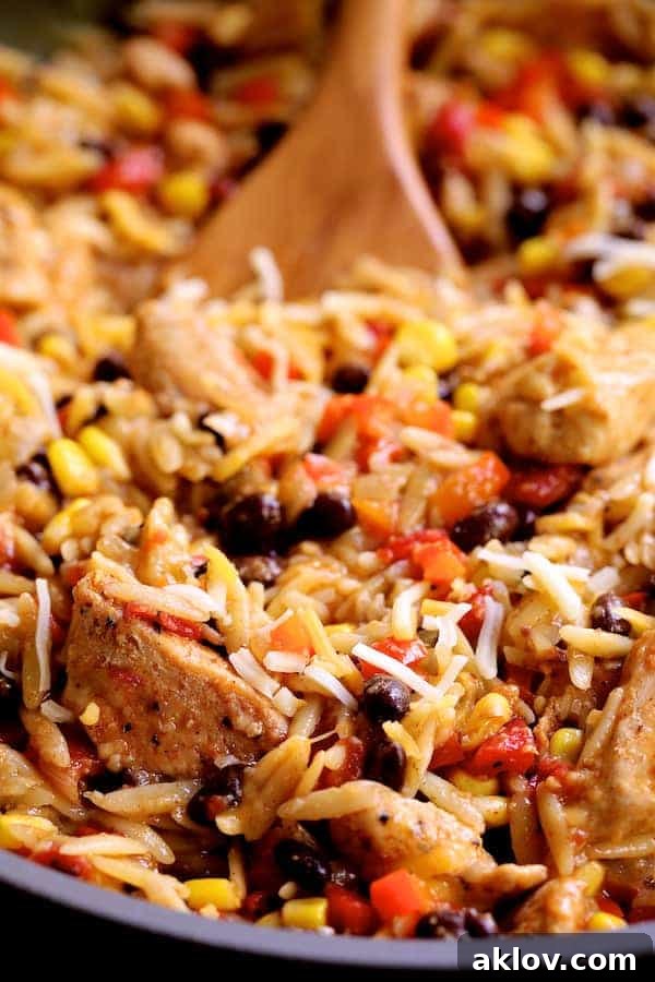 A close-up, appetizing view of the finished Southwestern Chicken Orzo and Black Bean Skillet, showcasing its rich texture and melted cheese.