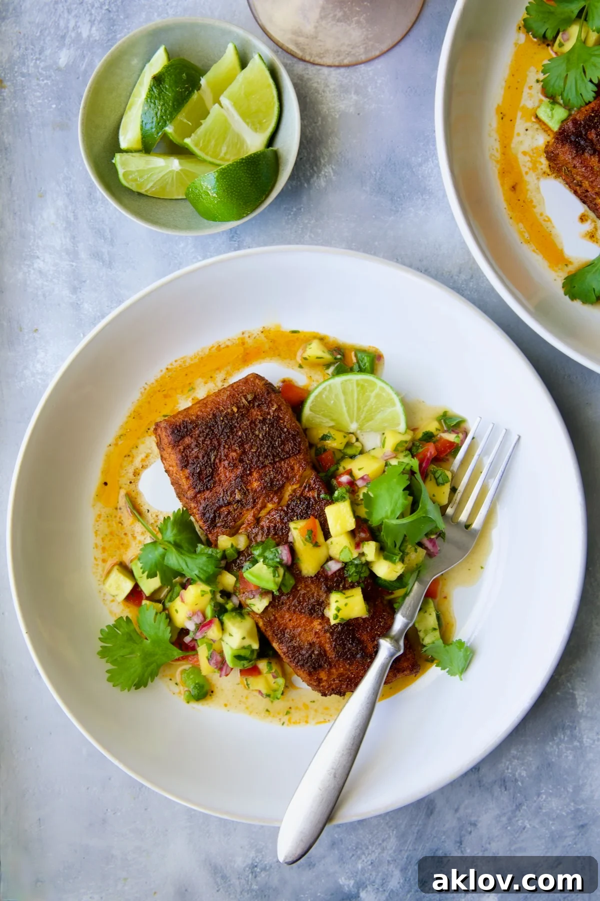 Blackened Halibut with Mango - Avocado Salsa on white plate with fork garnished with cilantro and lime wedge.
