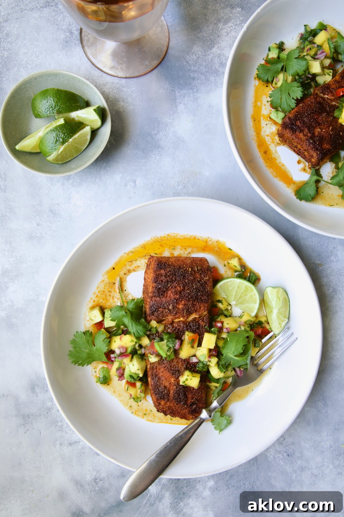 Two servings of Blackened Halibut with Mango - Avocado Salsa on white plates garnished with cilantro and lime wedge.
