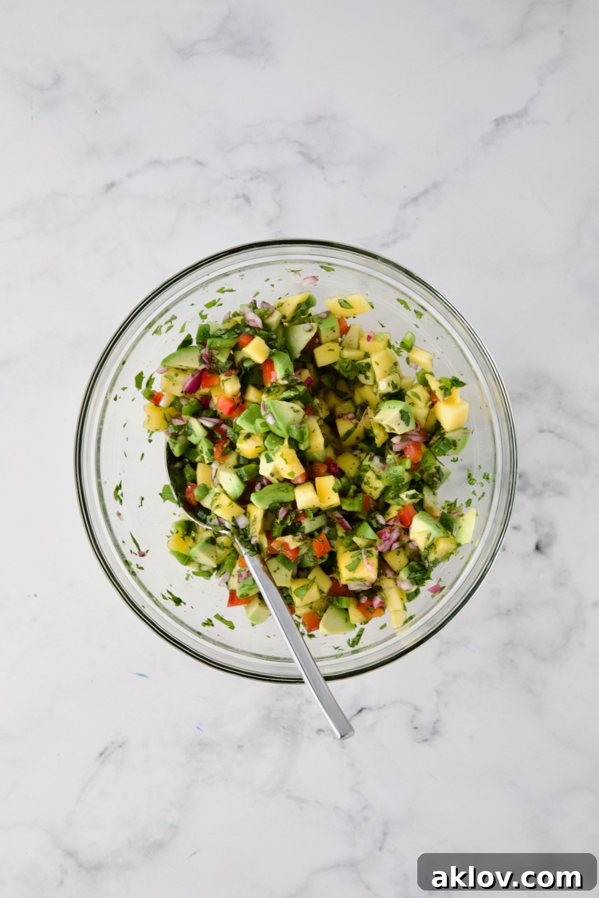 Ingredients for mango and avocado salsa in glass bowl after being stirred together with spoon.