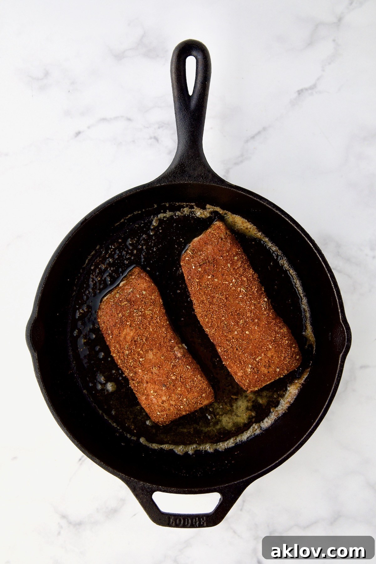 Two pieces of halibut coated with blackening seasoning in cast iron skillet.