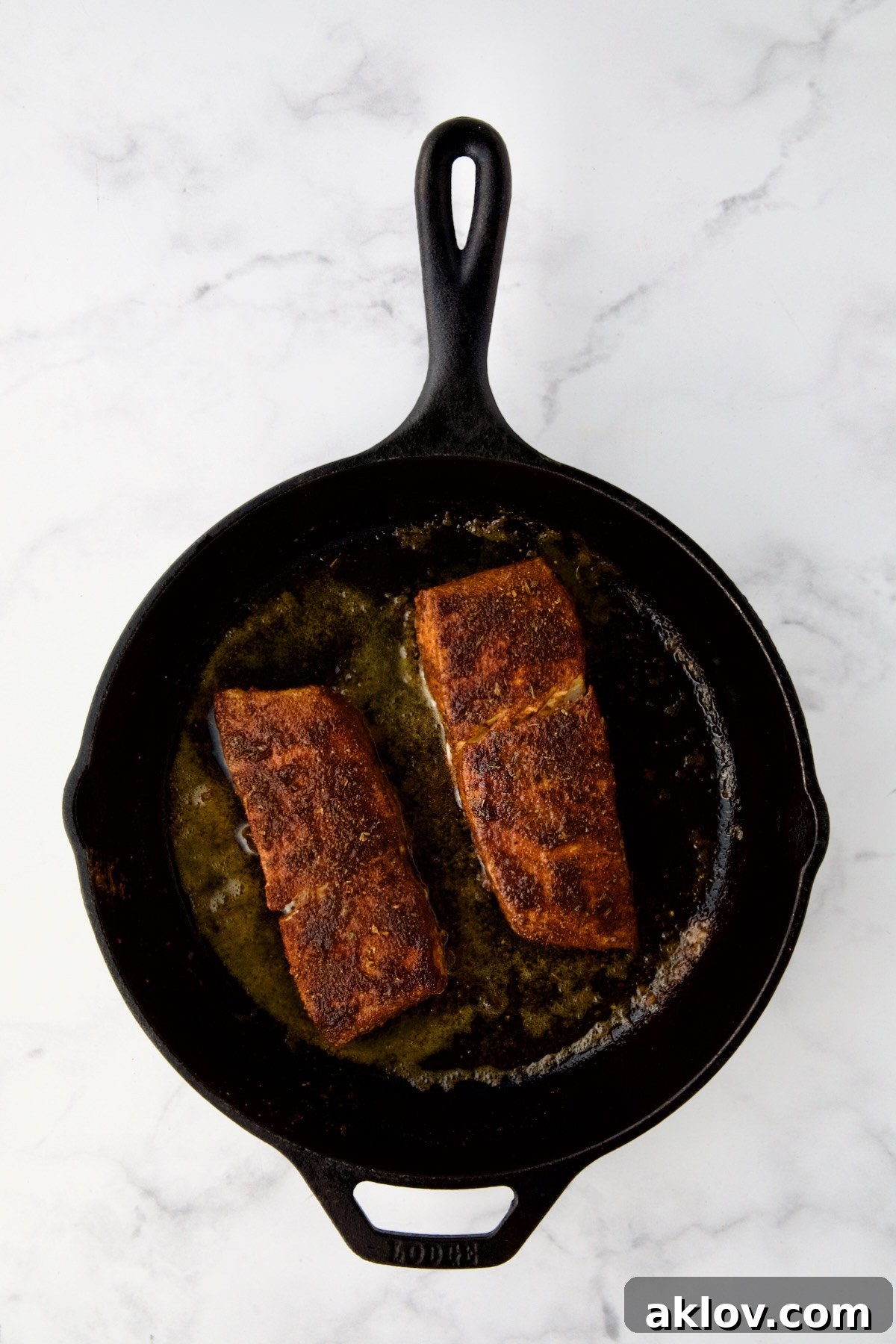 Two pieces of halibut coated with blackening seasoning in cast iron skillet after being cooked.