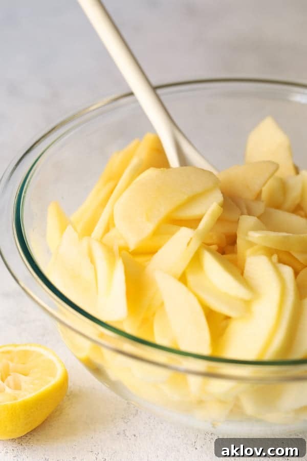 Photo of freshly sliced apples in glass bowl being stirred with white spoon.