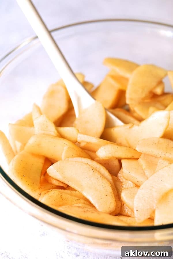 Photo of apples tossed with sugars and spices in glass bowl.
