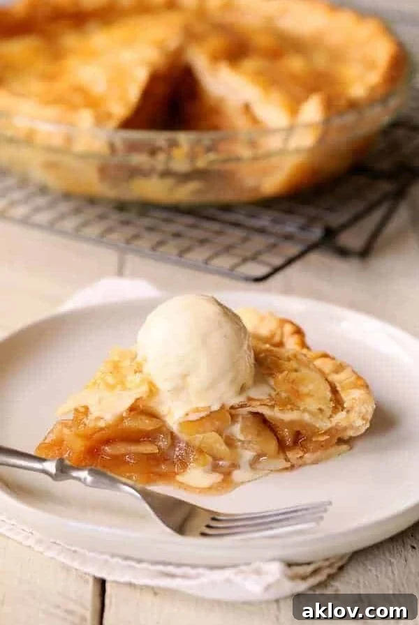 Slice of apple pie on white plate with vanilla ice cream.