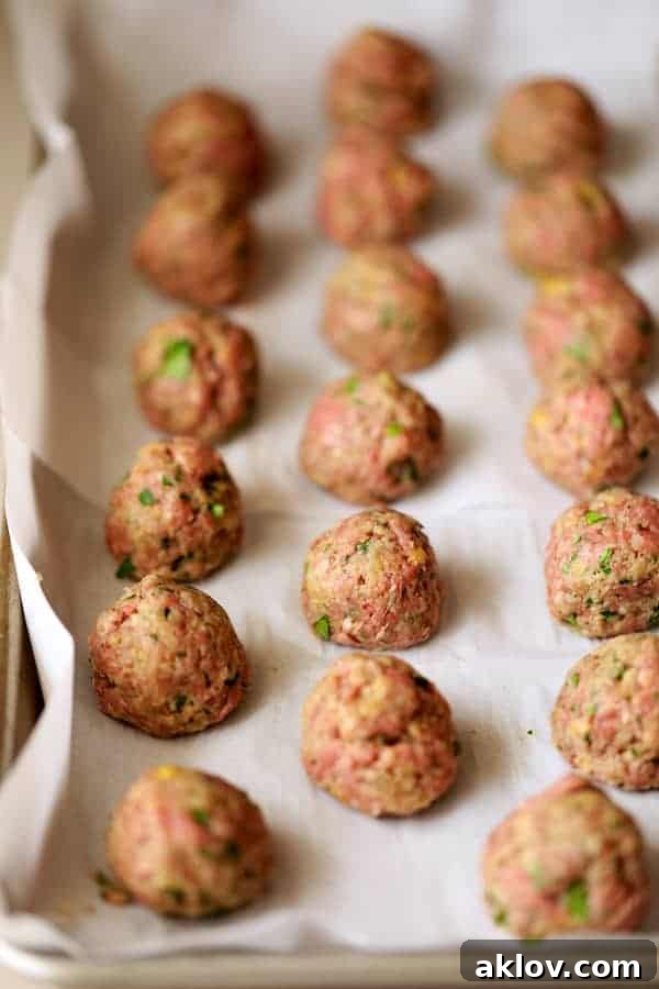 Photo of unbaked meatballs on parchment paper lined up in rows.