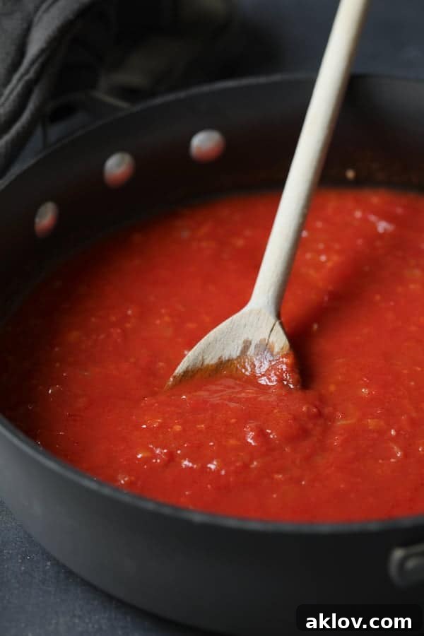 Photo of tomato sauce in skillet being stirred with wooden spoon.