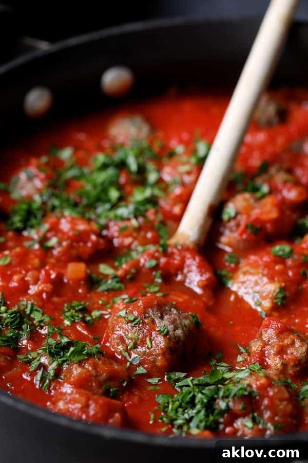 Photo of Middle Eastern Meatballs in Tomato Sauce in skillet being stirred with wooden spoon.