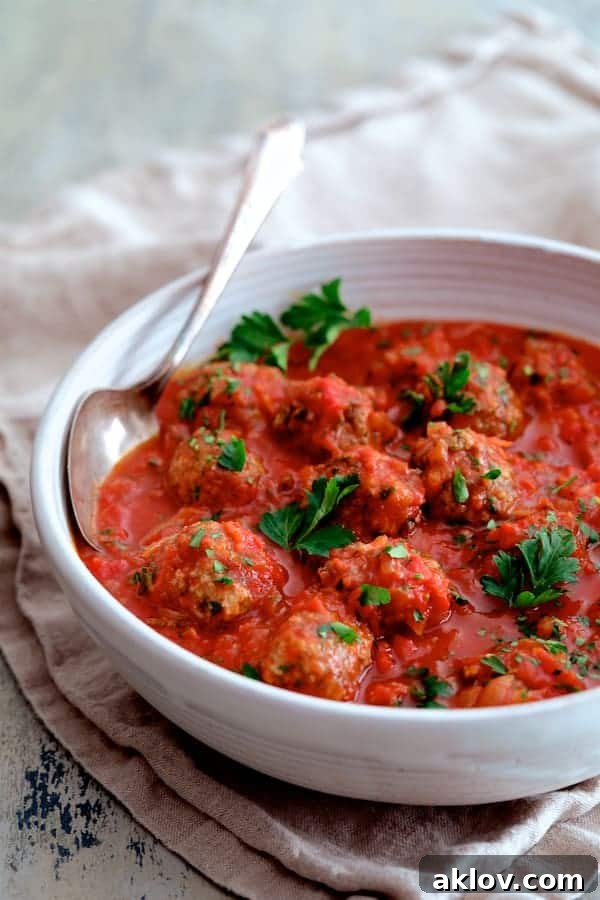 Photo of Middle Eastern Meatballs in Tomato Sauce in white serving bowl with serving spoon garnished with parsley.