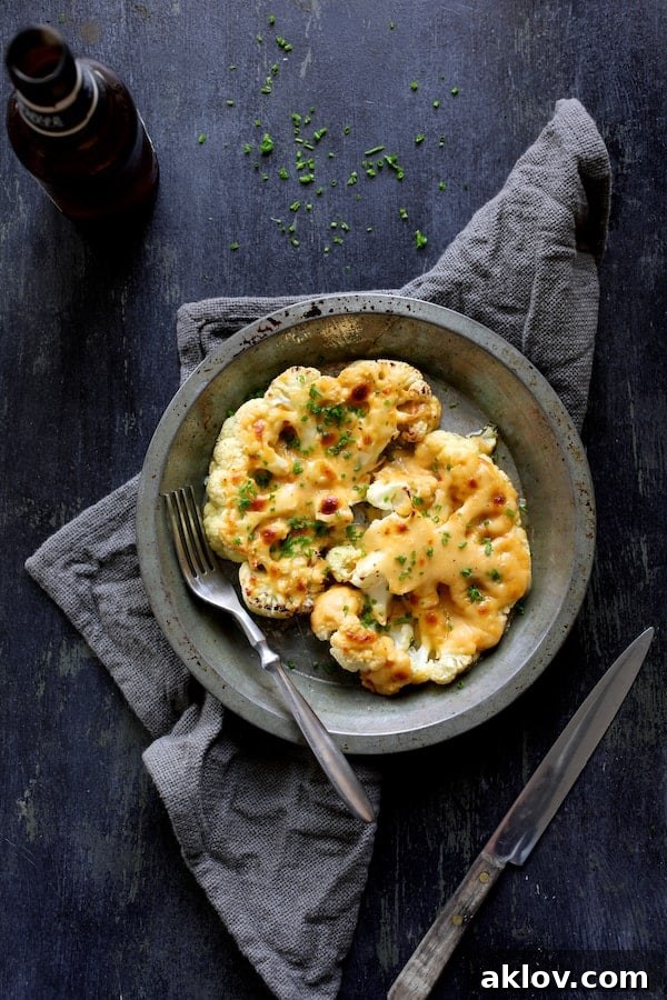 A serving of Cauliflower Welsh Rarebit in a metal dish, set against a blue background with a gray napkin, highlighting its rustic appeal.